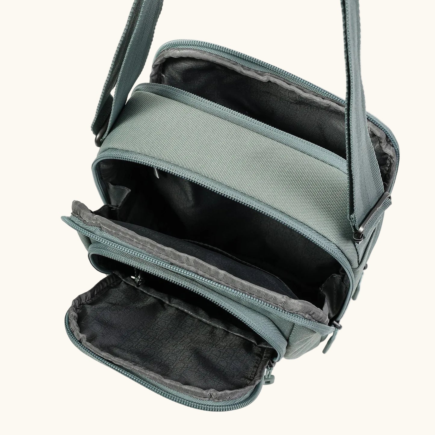 Light sage green sling bag by Hedgren with multiple open zippered compartments and an adjustable strap.
