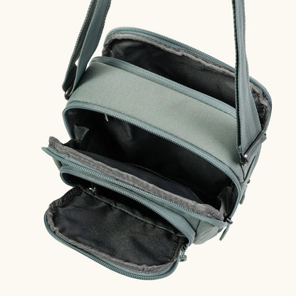 Light sage green sling bag by Hedgren with multiple open zippered compartments and an adjustable strap.
