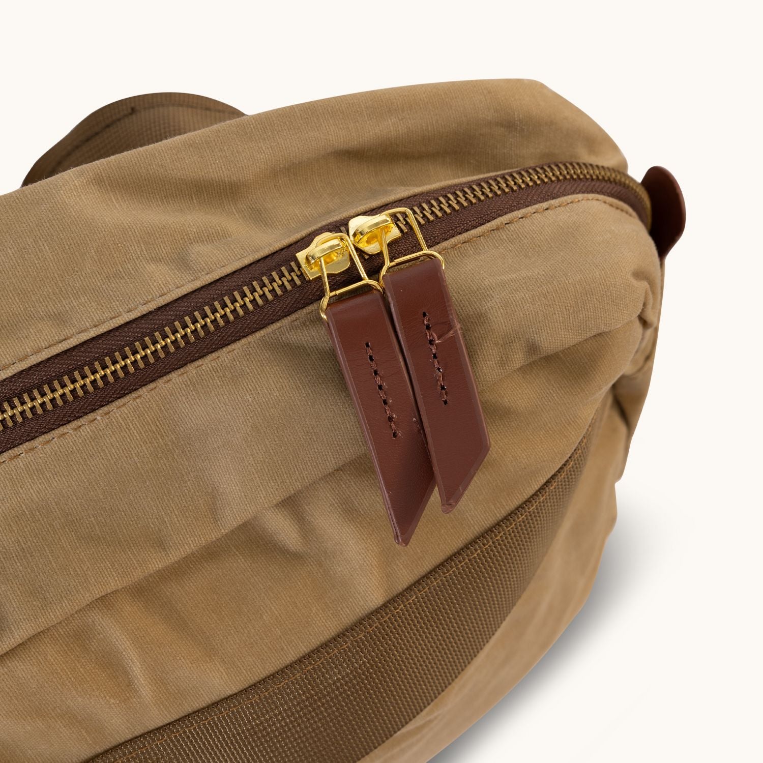 Large Utility Tan waxed canvas crossbody bag with a brown zipper, gold pulls, and brown leather tabs.
