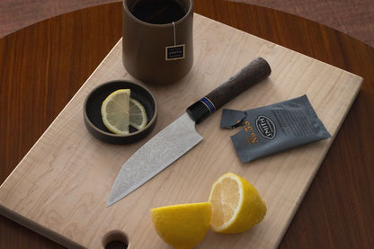 Light maple wood cutting board with a circular hole, styled with a chef's knife, tea, and sliced lemons.