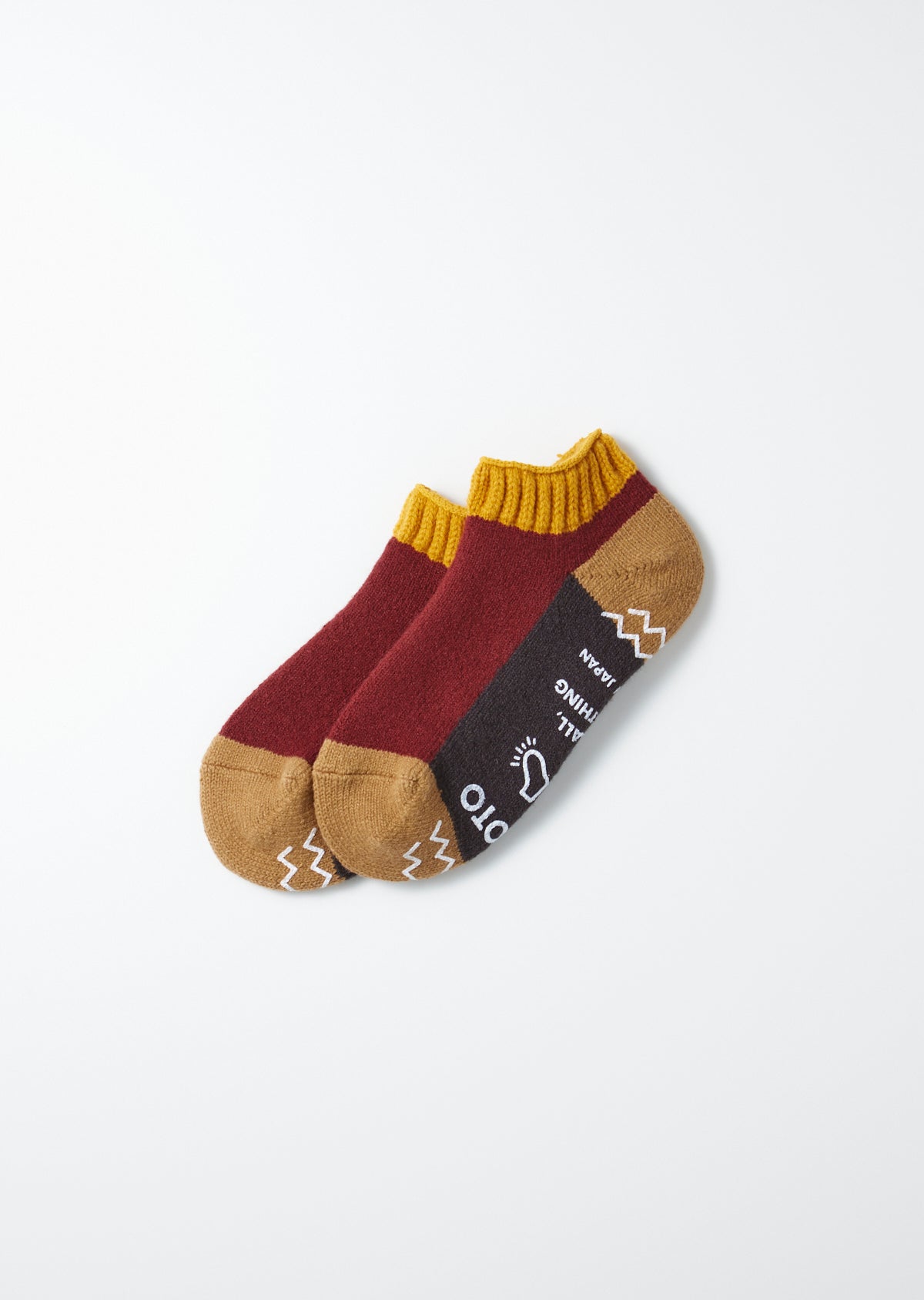 Two maroon and brown pile sockslippers with mustard yellow ribbed cuffs, a dark stripe, and white zigzag patterns on the toes.