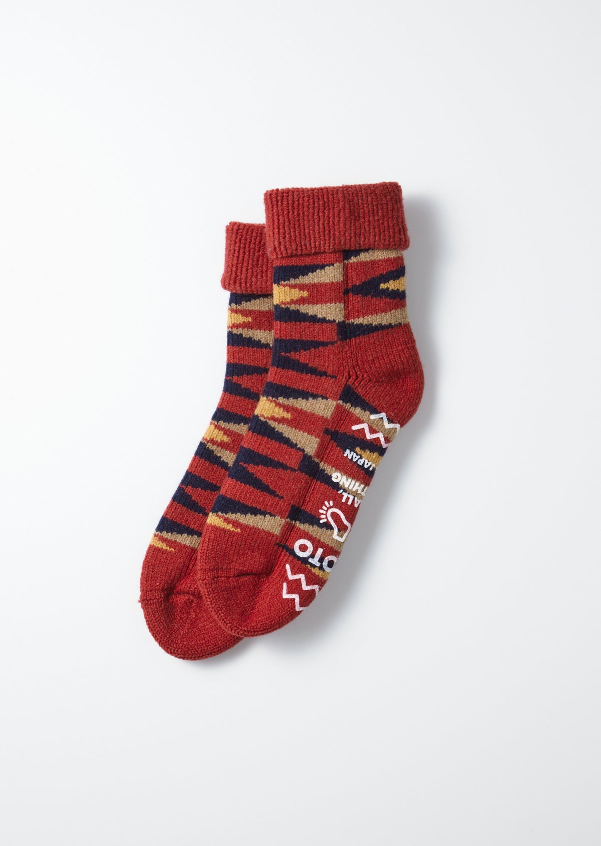 A pair of red Merino Lamb Wool room socks featuring a native geometric pattern in navy, tan, and yellow, with white graphic text and symbols on the side.