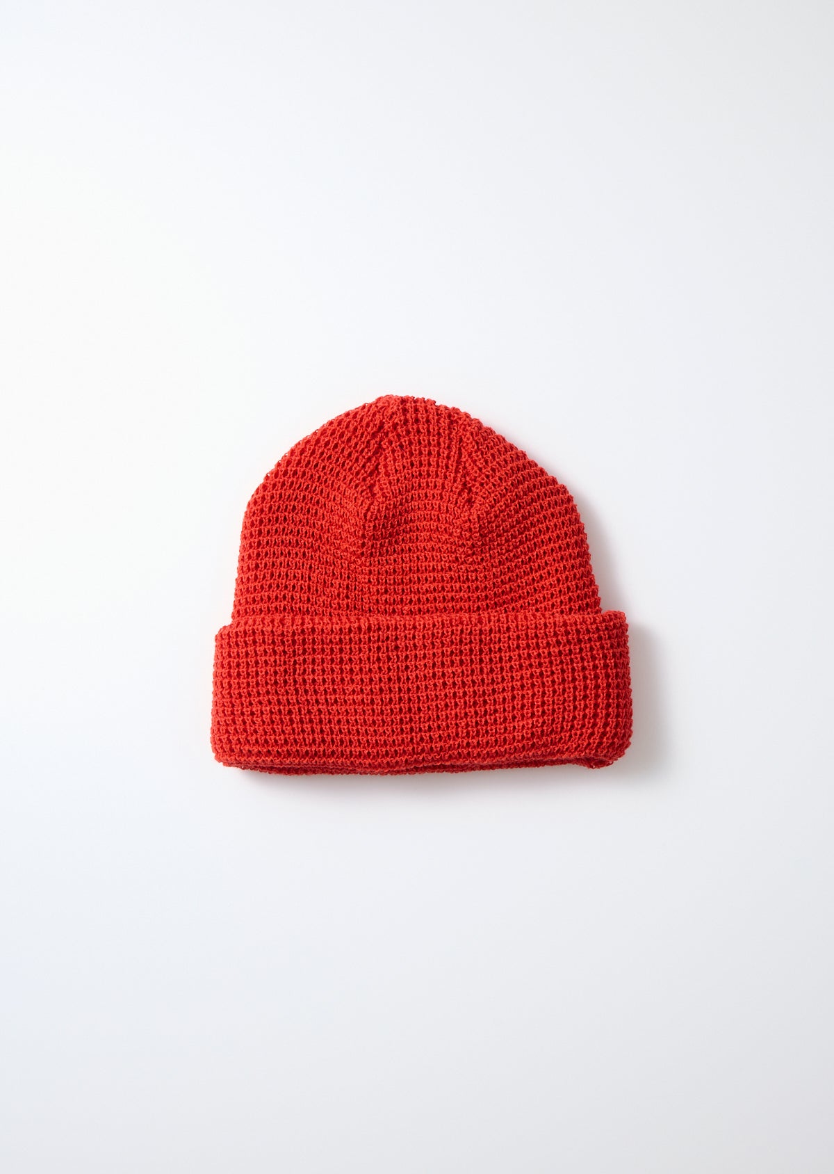 Red waffle knit watch cap with a folded brim, laid flat on a white background.