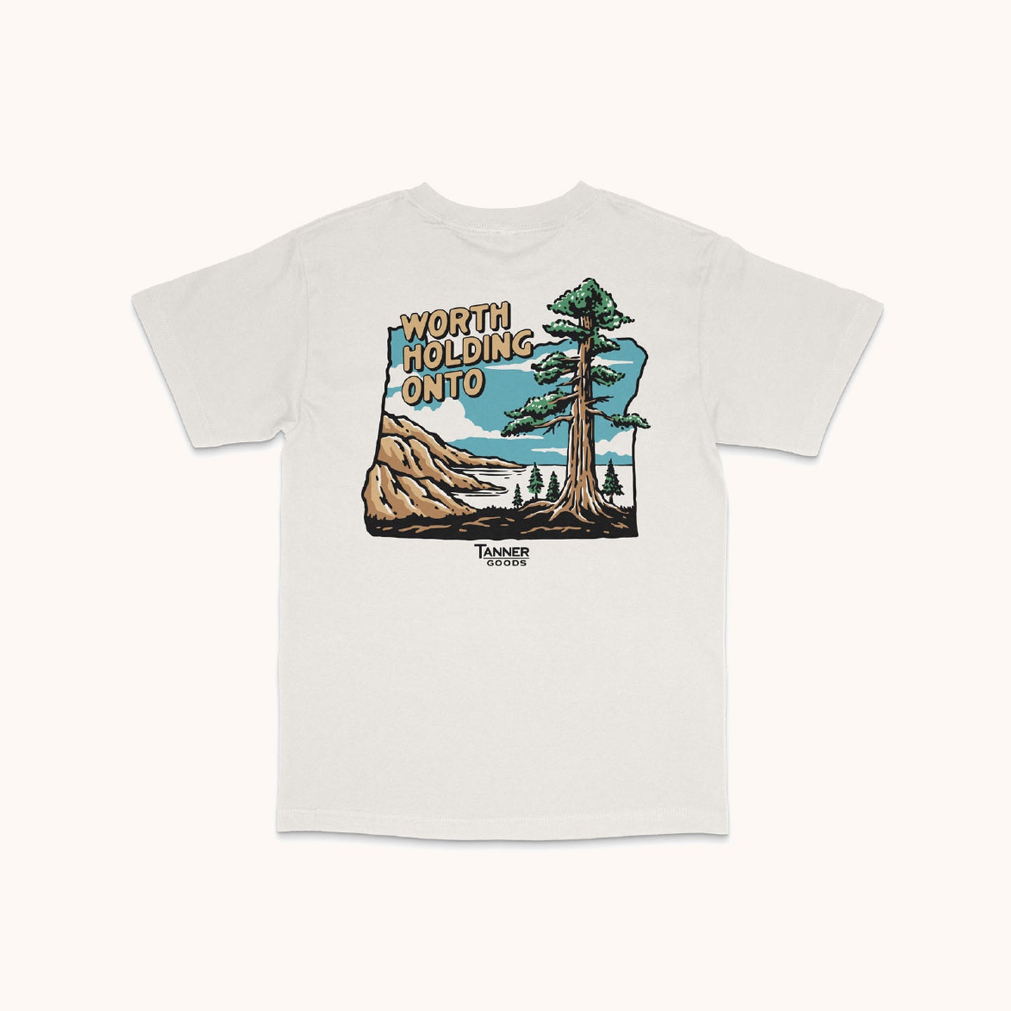 White Adventure T-Shirt by TANNER GOODS with a back graphic of mountains, a lake, a large tree, and "WORTH HOLDING ONTO" text.
