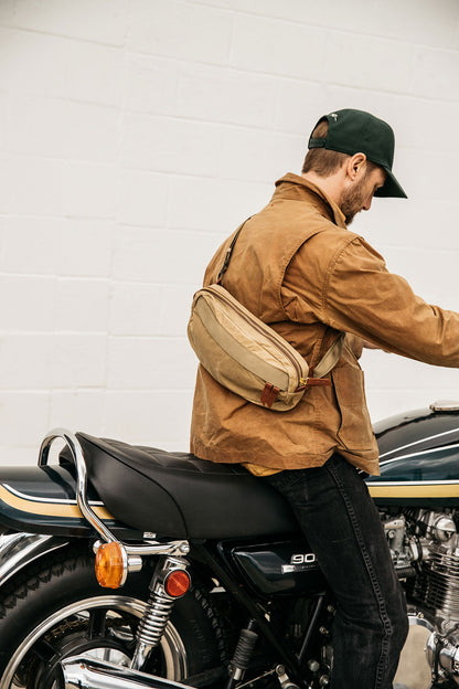 Utility Tan Waxed Canvas Canyon Crossbody Pack worn across a man's back on a vintage motorcycle.