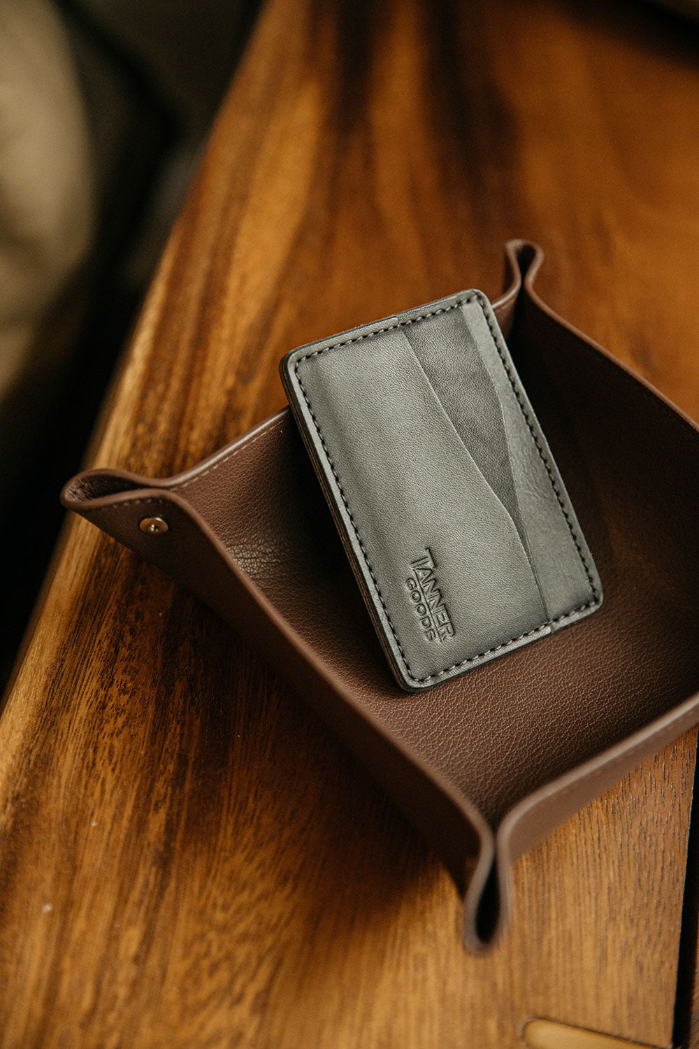 Cognac recycled leather valet tray with snapped corners, holding a grey leather card holder, on a wooden surface.