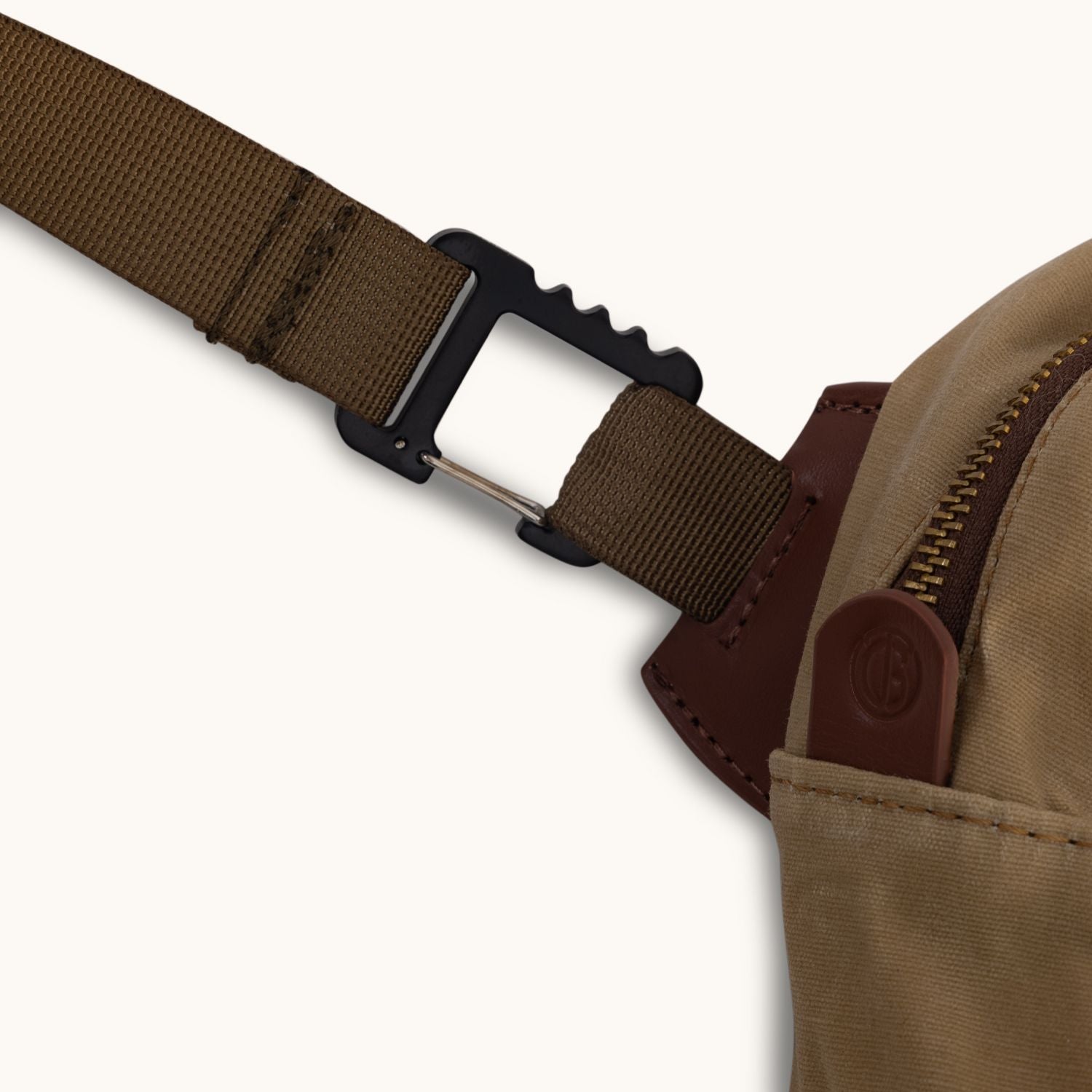 Tan waxed canvas crossbody bag with a brown strap, black carabiner, and leather pull with embossed logo.