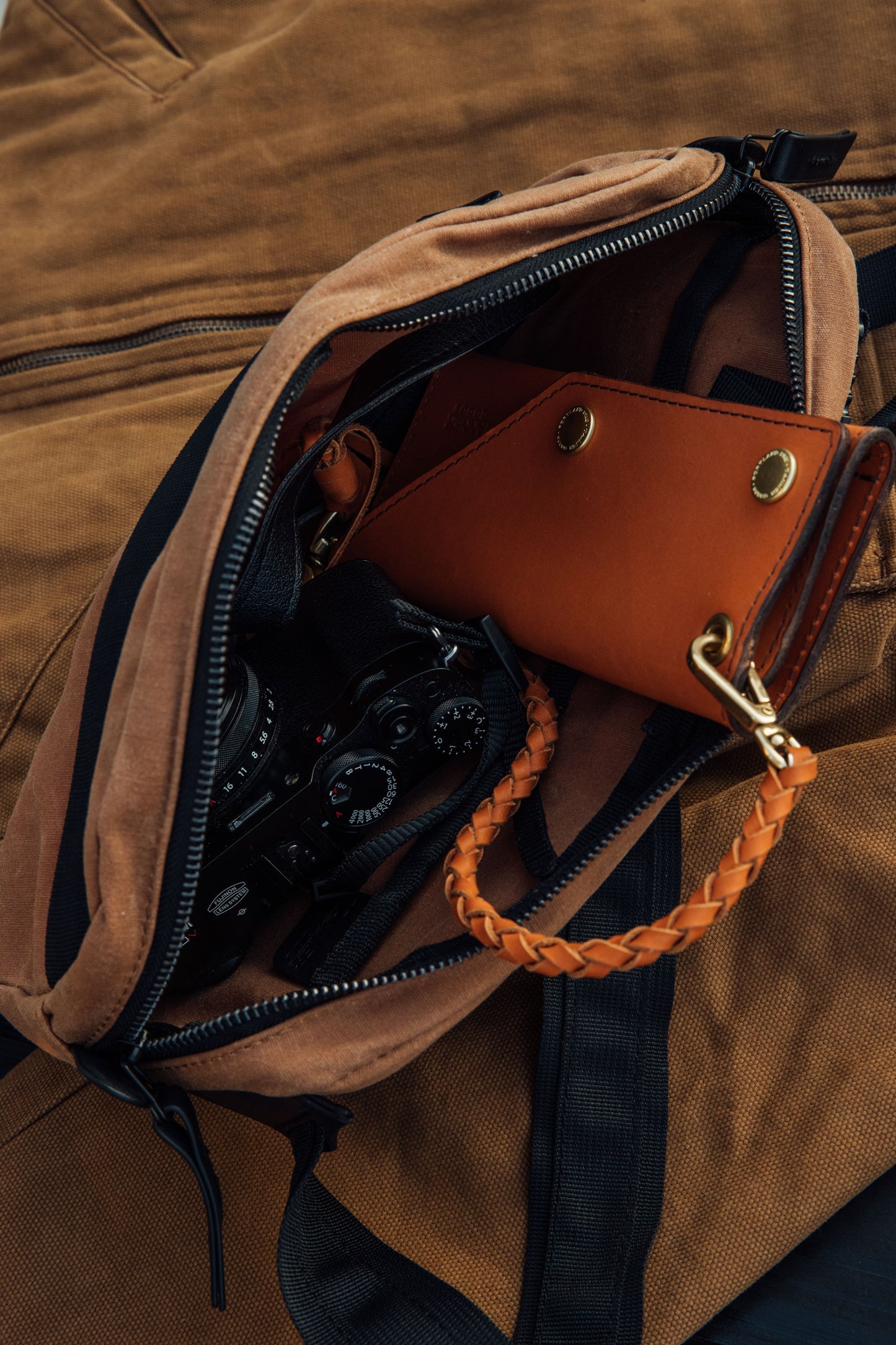 Desert Rose Waxed Canvas Crossbody Pack, open to show a black camera, brown leather wallet, and braided leather strap inside.