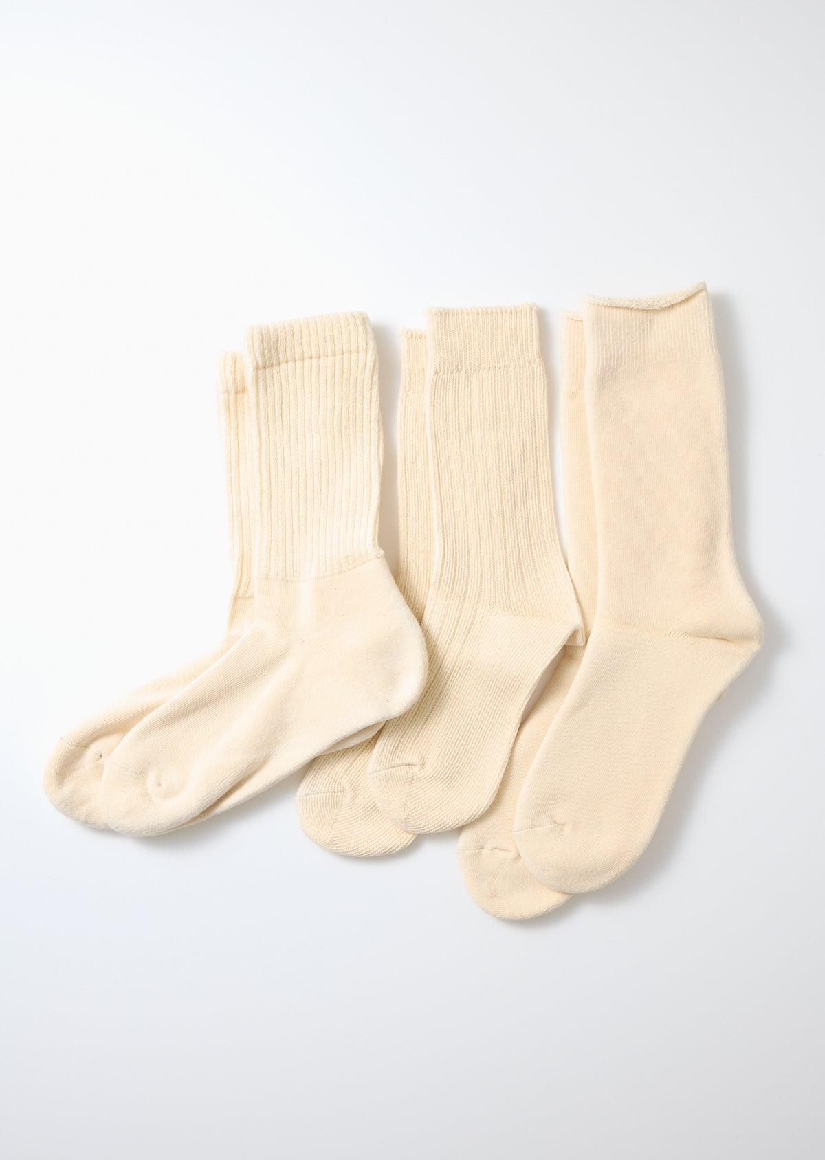 Three pairs of ecru knit crew socks featuring ribbed legs, laid flat on a white surface.