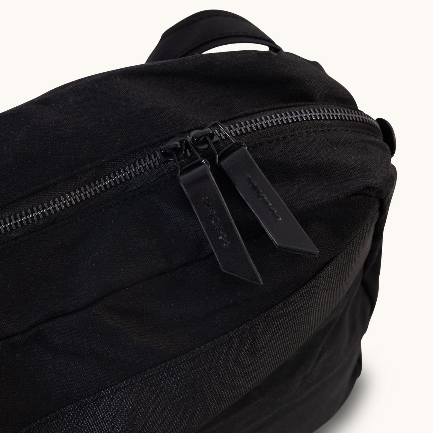 Large onyx waxed canvas Canyon crossbody bag, angled close-up showing two black zipper pull tabs and a side strap.