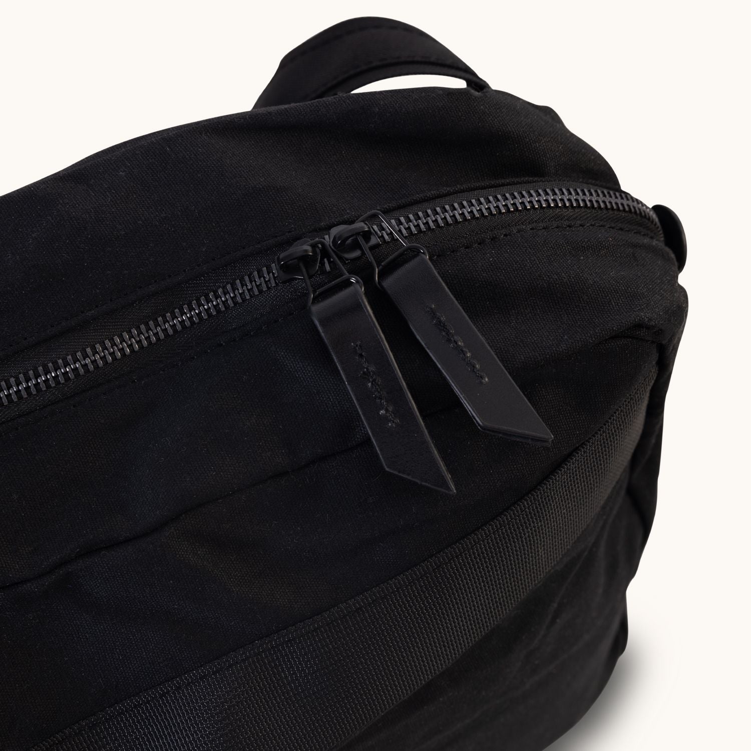 Large onyx waxed canvas Canyon crossbody bag, angled close-up showing two black zipper pull tabs and a side strap.