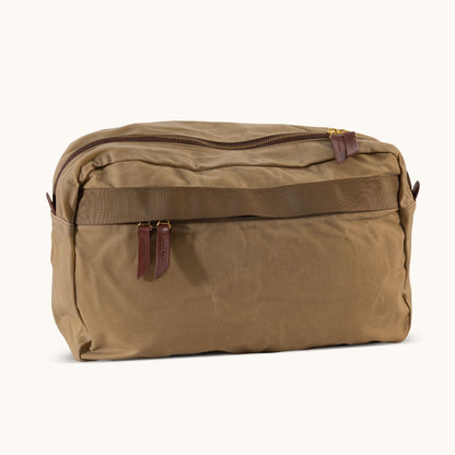 A large utility tan waxed canvas crossbody bag with a zippered top, two brown leather pulls, and a front horizontal strap.
