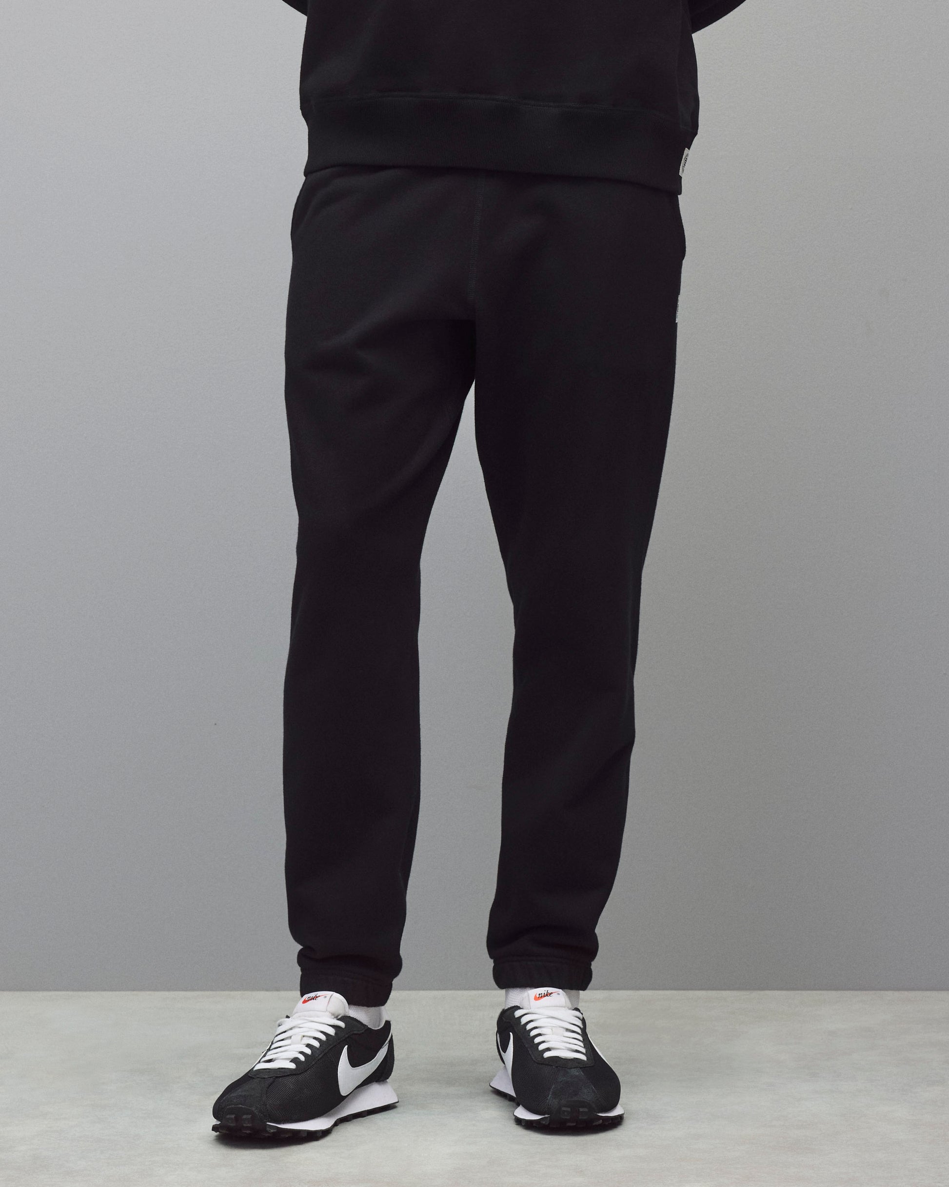 Black midweight terry standard sweatpants featuring a ribbed waistband and cuffs, worn with white socks and black sneakers.