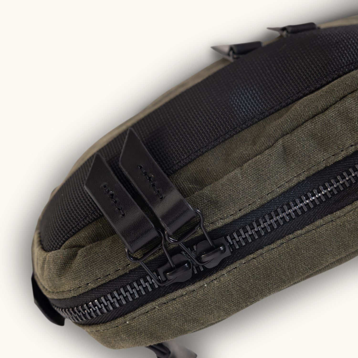 Juniper Green waxed canvas Canyon Crossbody Mini featuring a black woven top panel and dual black zippers with leather pull tabs.