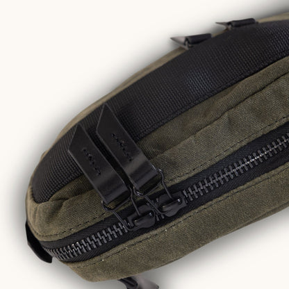 Juniper Green waxed canvas Canyon Crossbody Mini featuring a black woven top panel and dual black zippers with leather pull tabs.