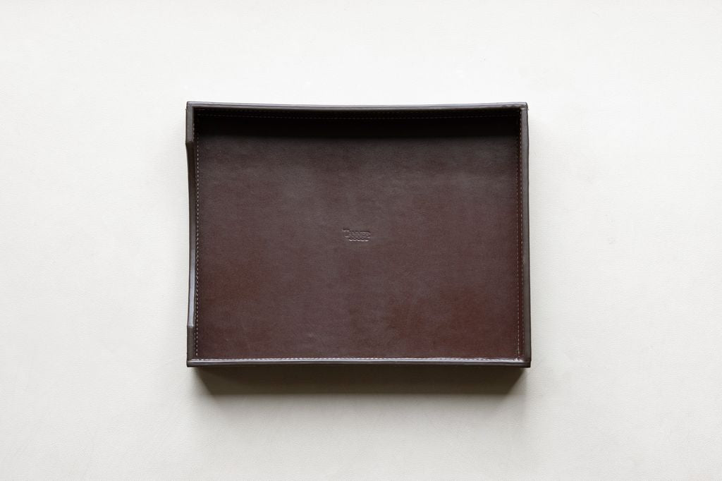 Dark brown leather paper tray with visible white stitching and a subtle embossed "Tanner" text in the center.