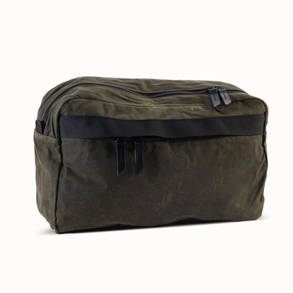 Juniper green waxed canvas crossbody bag with a black front strap and dual zipper pulls.