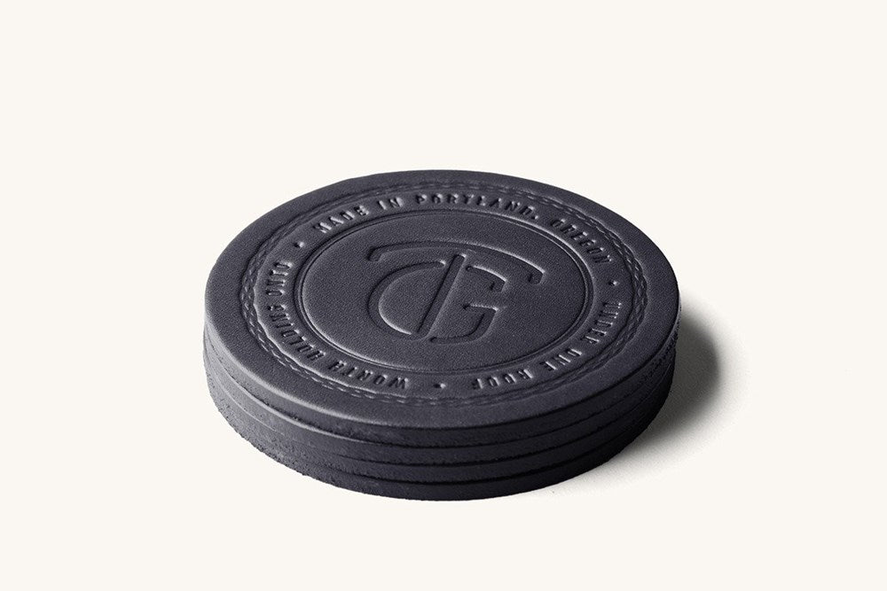 Black round leather coaster set by TG, stacked, featuring an embossed logo and circular text.
