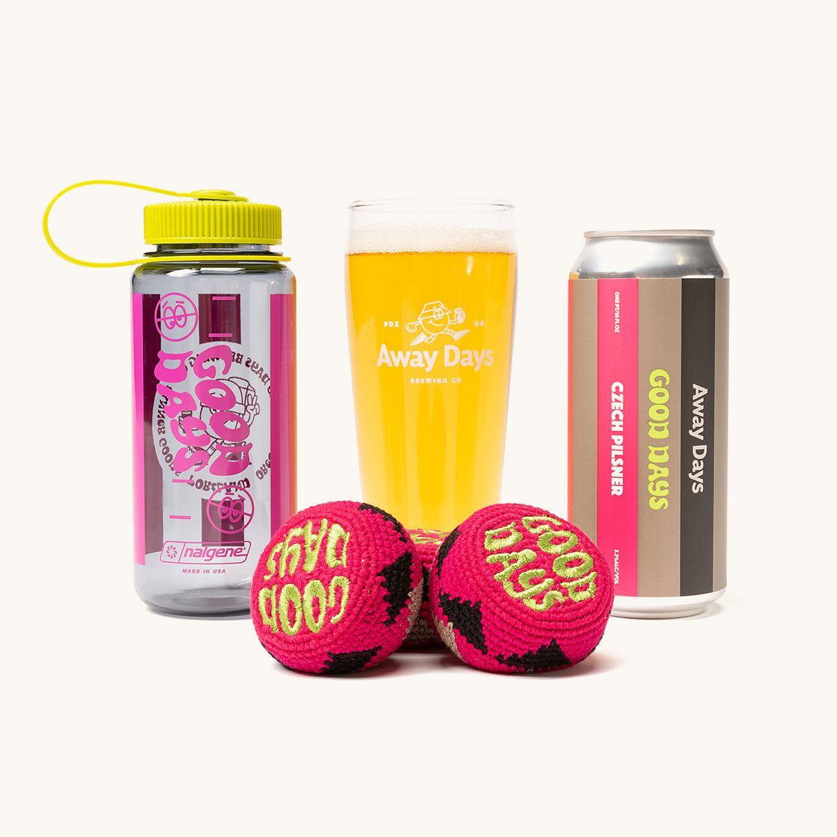 A pair of pink and black crocheted footbags with "GOOD DAYS" text, displayed with a clear water bottle, a glass of beer, and a beer can.