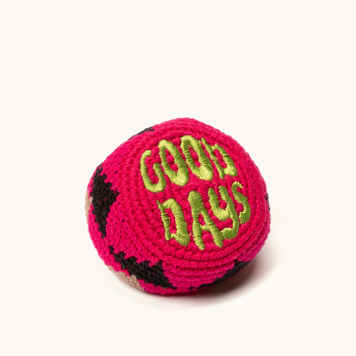 Hot pink crocheted footbag with lime green "GOOD DAYS" embroidery, accented with black and beige patches, viewed at an angle.