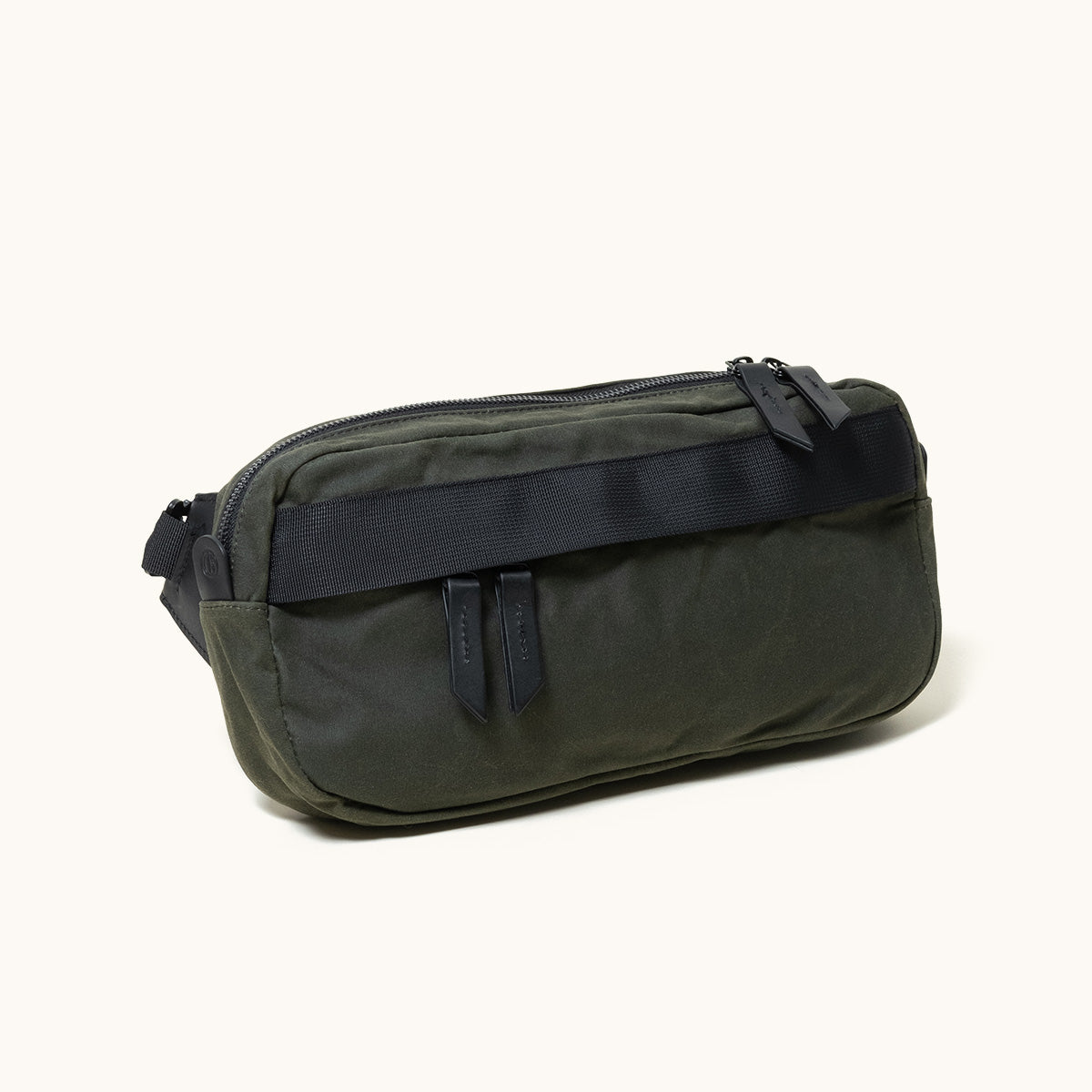 Dark green crossbody bag with a zippered main compartment, two front vertical zip pockets, and a black woven strap across the front.