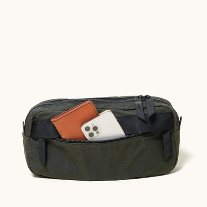 Juniper Green waxed canvas crossbody pack, open to show a brown wallet and a silver smartphone.