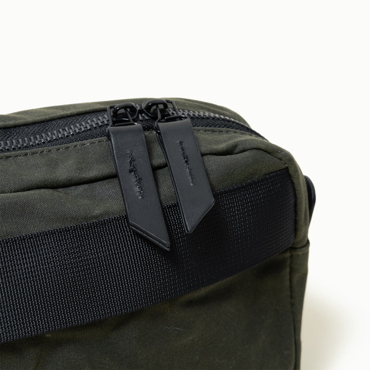 Juniper Green waxed canvas Canyon Crossbody Pack with black zipper, two black leather pulls, and black webbing.