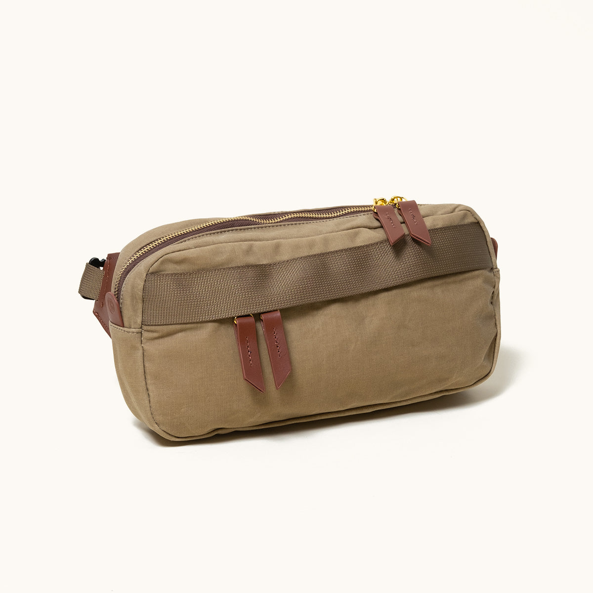 Olive green canvas sling bag with two front pockets, brown leather zipper pulls, and gold zippers, angled on a white background.