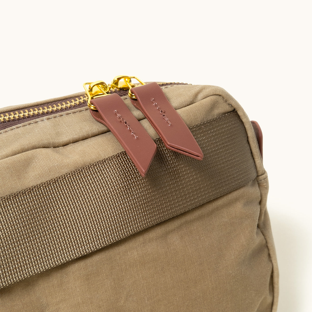 Utility Tan Waxed Canvas Crossbody Pack with gold zippers, brown woven strap, and brown embossed pull tabs.