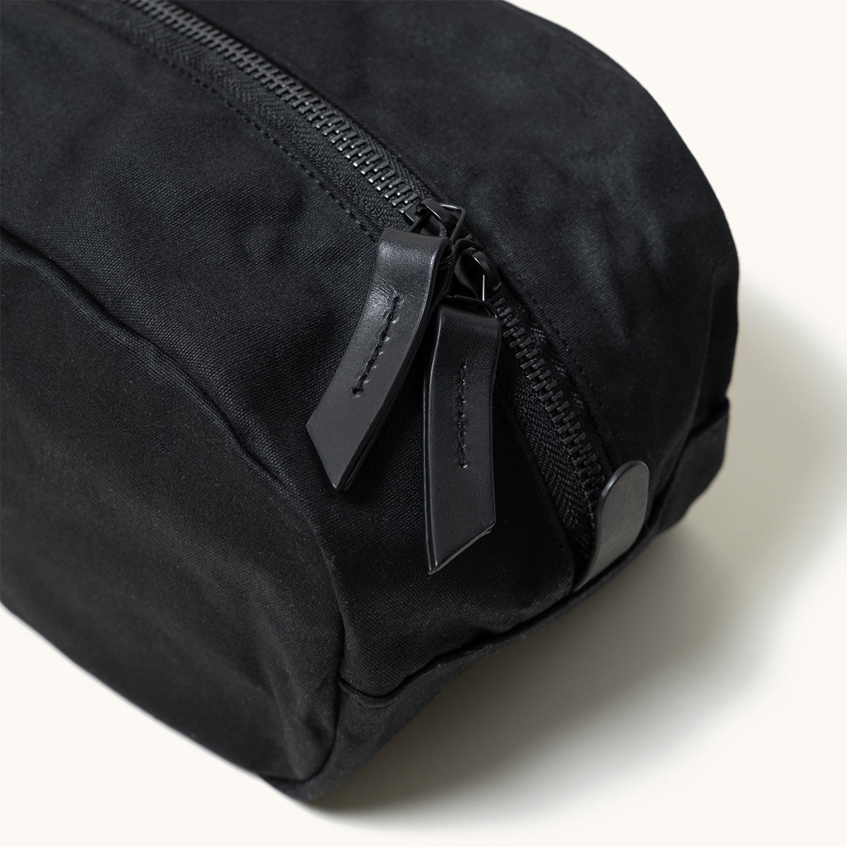 Black waxed canvas Drifter Dopp Kit with metal zipper and two black leather pulls, angled close-up.