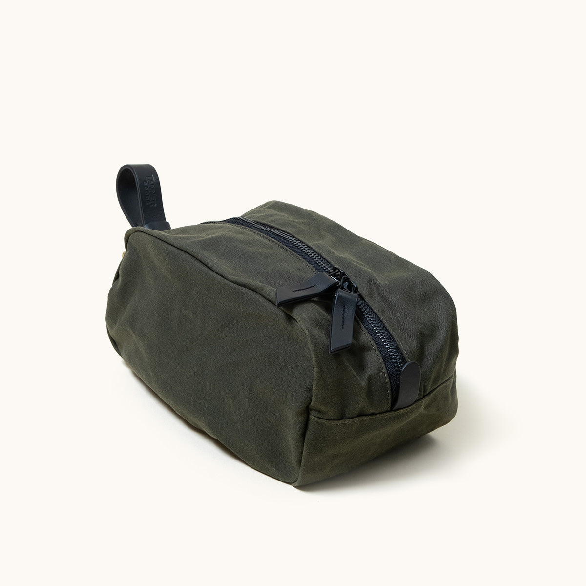 Dark green waxed canvas Drifter Dopp Kit with a black zipper, two leather pull tabs, and a leather carry loop, shown at an angle.