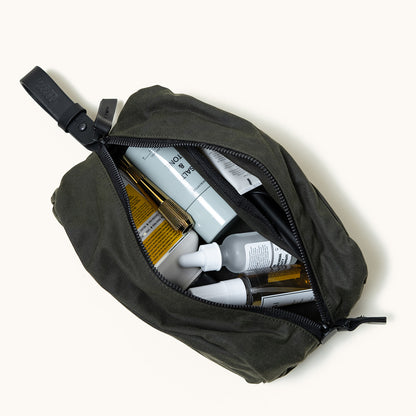 Juniper green waxed canvas Dopp kit by Tanner Goods, open with various skincare products inside.