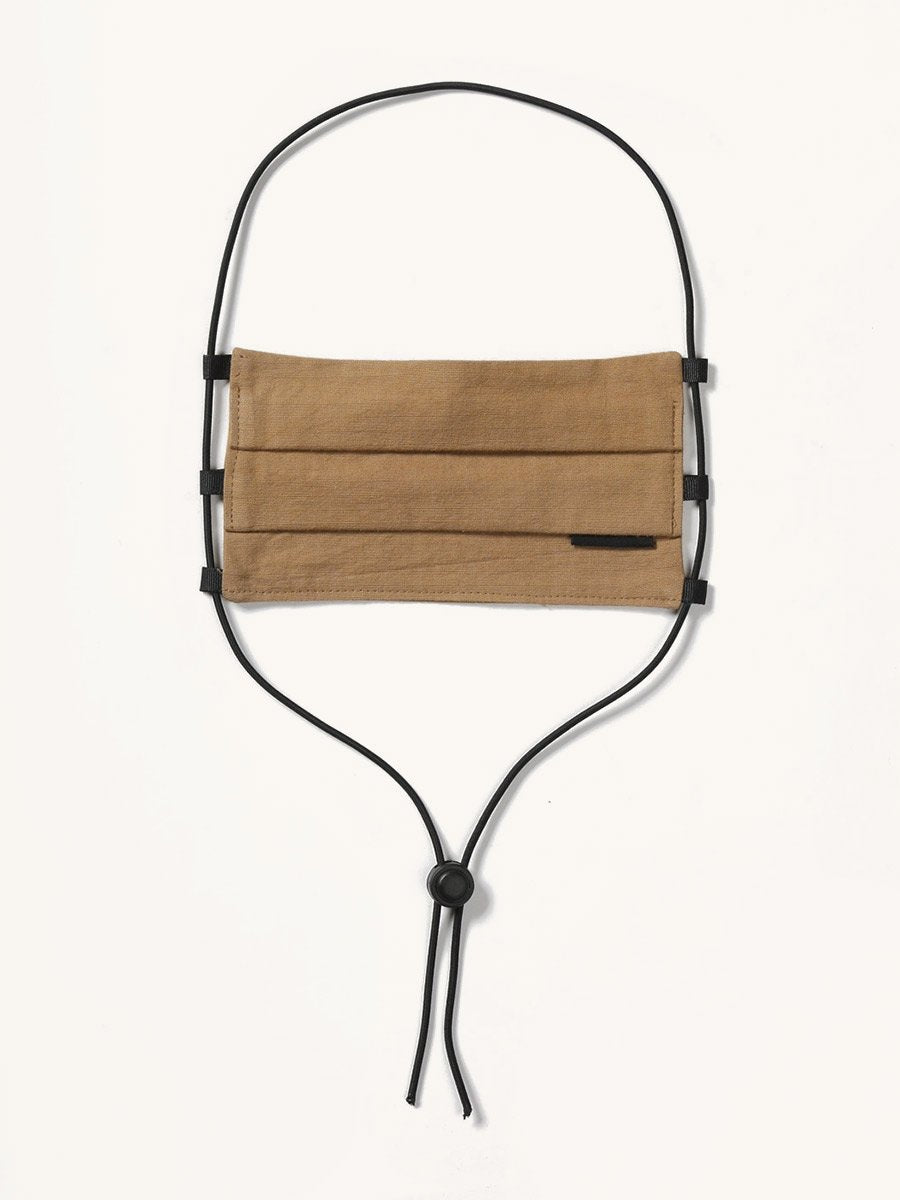 Brown fabric face covering with pleats, featuring a small black tag and black adjustable cords, hanging against a white background.