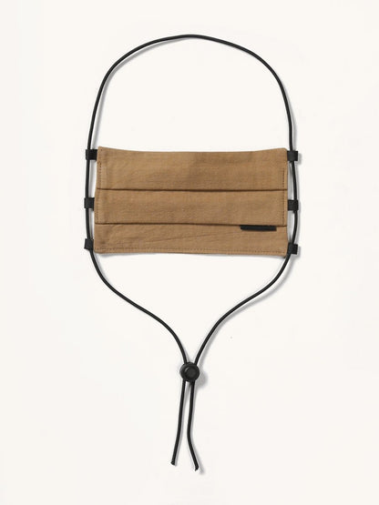 Brown fabric face covering with pleats, featuring a small black tag and black adjustable cords, hanging against a white background.