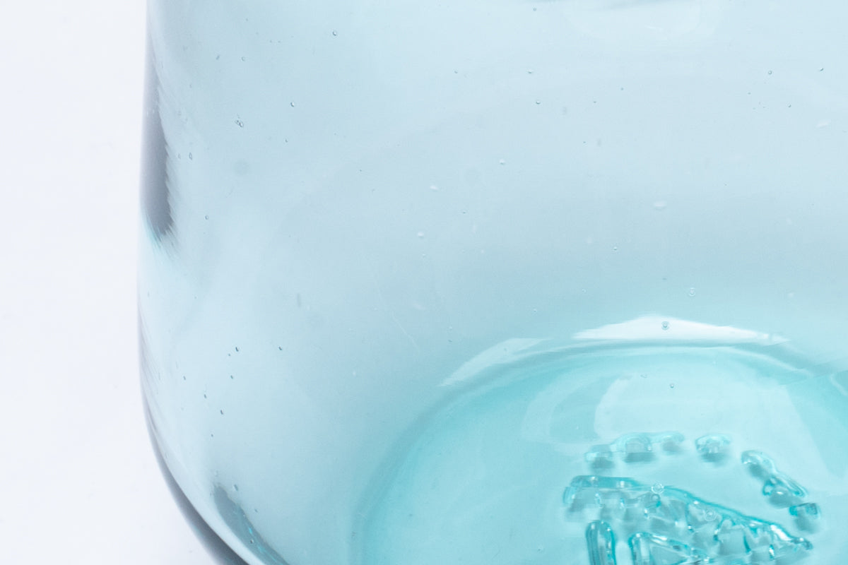 Light blue cocktail glass, close-up showing small air bubbles embedded in the glass and a textured, raised pattern on the inner bottom.