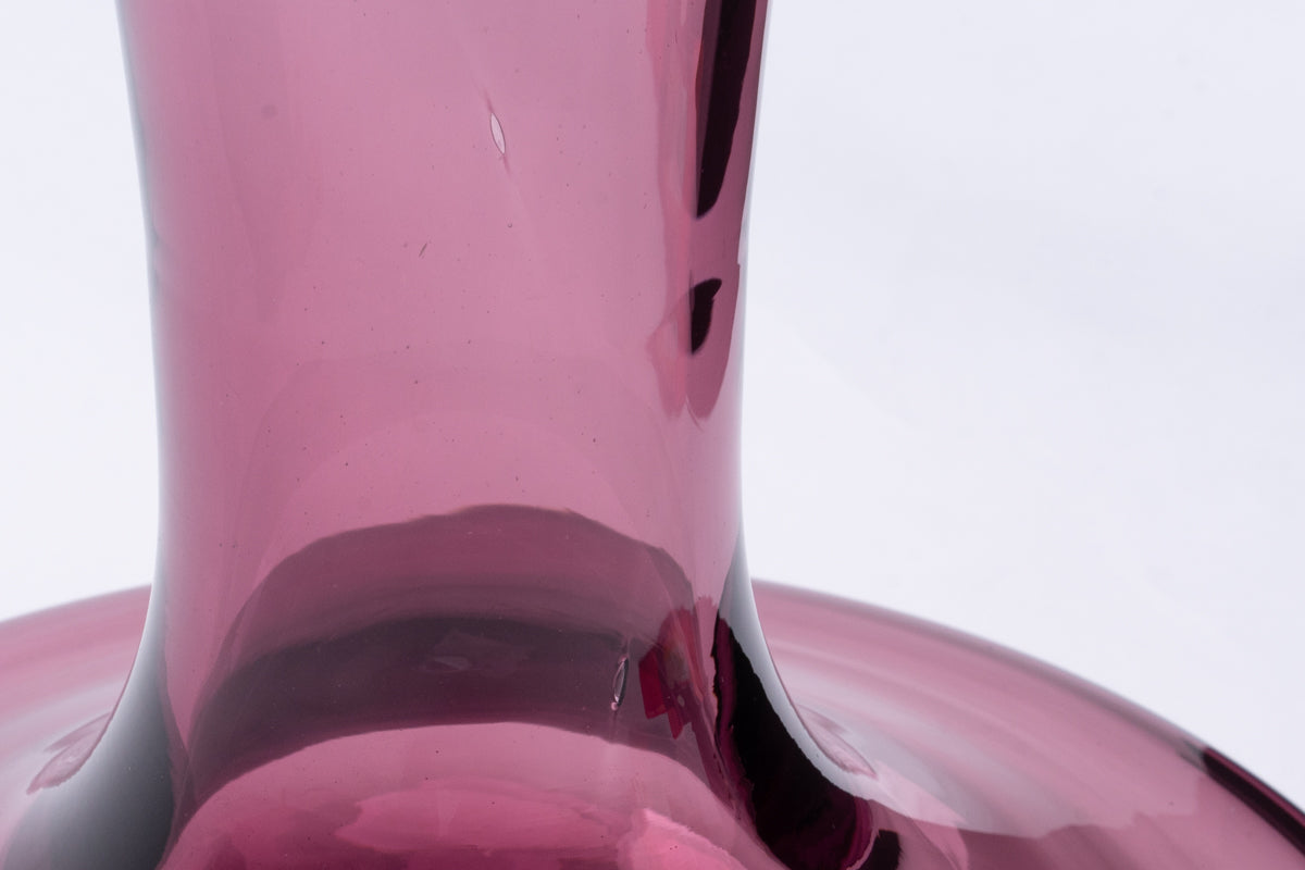 Purple glass decanter, a close-up showing its curved neck, wide base, and minor visible imperfections.