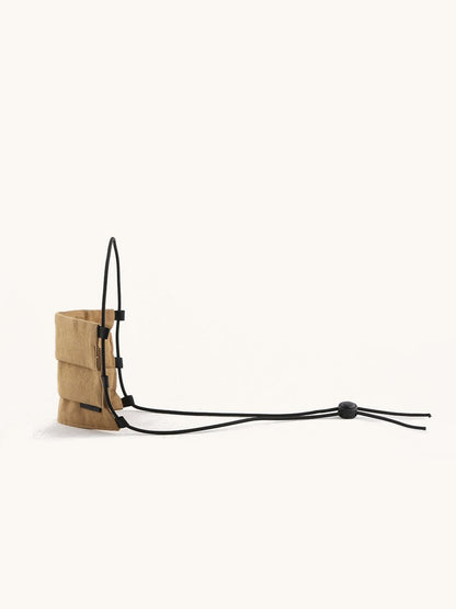 Tan fabric face covering with pleated details and long black adjustable cords, side view.
