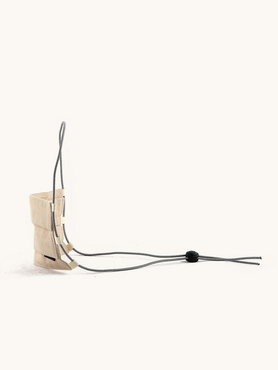Structured light beige fabric face covering with a black and white braided cord and an adjustable stopper.