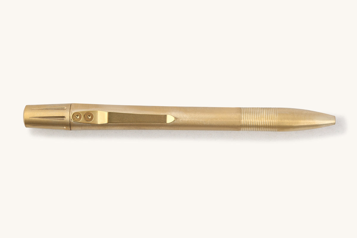 Brass pen with a ribbed grip, pocket clip attached by two screws, and a fluted cap, side view.