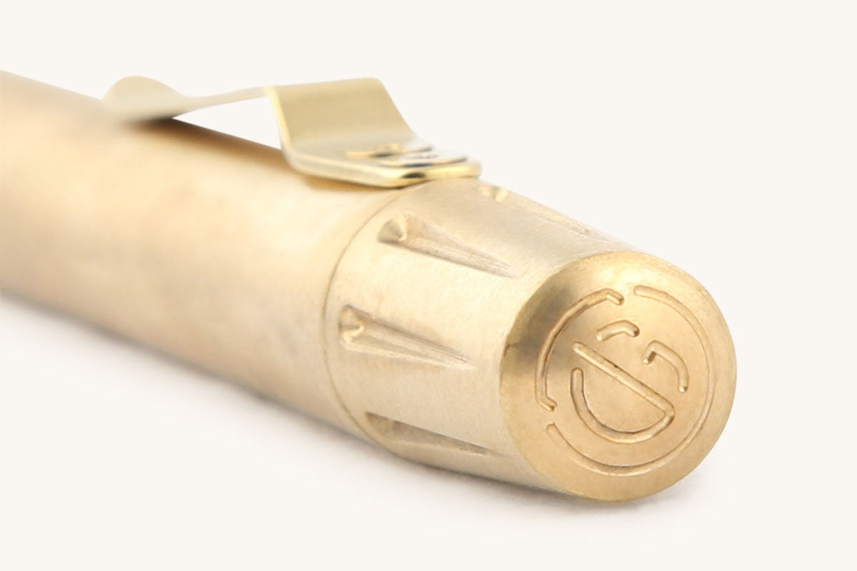 Brass Memori Mechanico with a gold-colored clip and an engraved logo on its textured end.