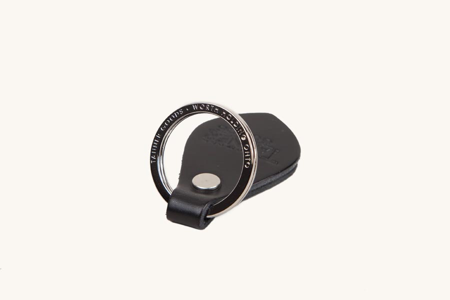 Black leather key fob with a silver metal ring engraved "TANNER GOODS WORTH HOLDING ONTO" and a silver snap.