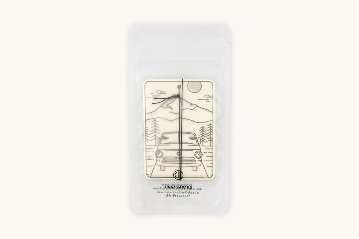 Off-white air freshener by Tanner Goods featuring a line art mountain and car scene labeled 'HIGH SABAKU', inside clear packaging.