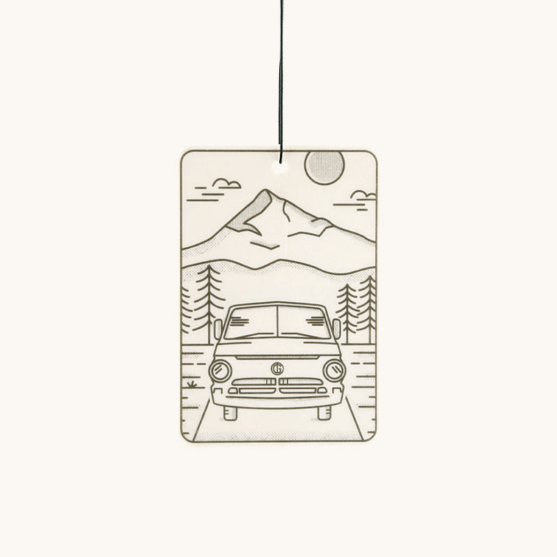 Off-white rectangular air freshener by Tanner Goods with a minimalist line art drawing of a mountain, trees, and a camper van.