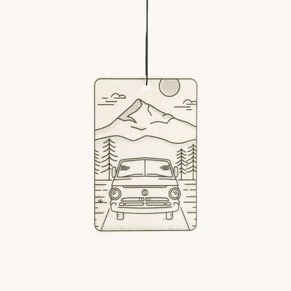 Off-white rectangular air freshener by Tanner Goods with a minimalist line art drawing of a mountain, trees, and a camper van.