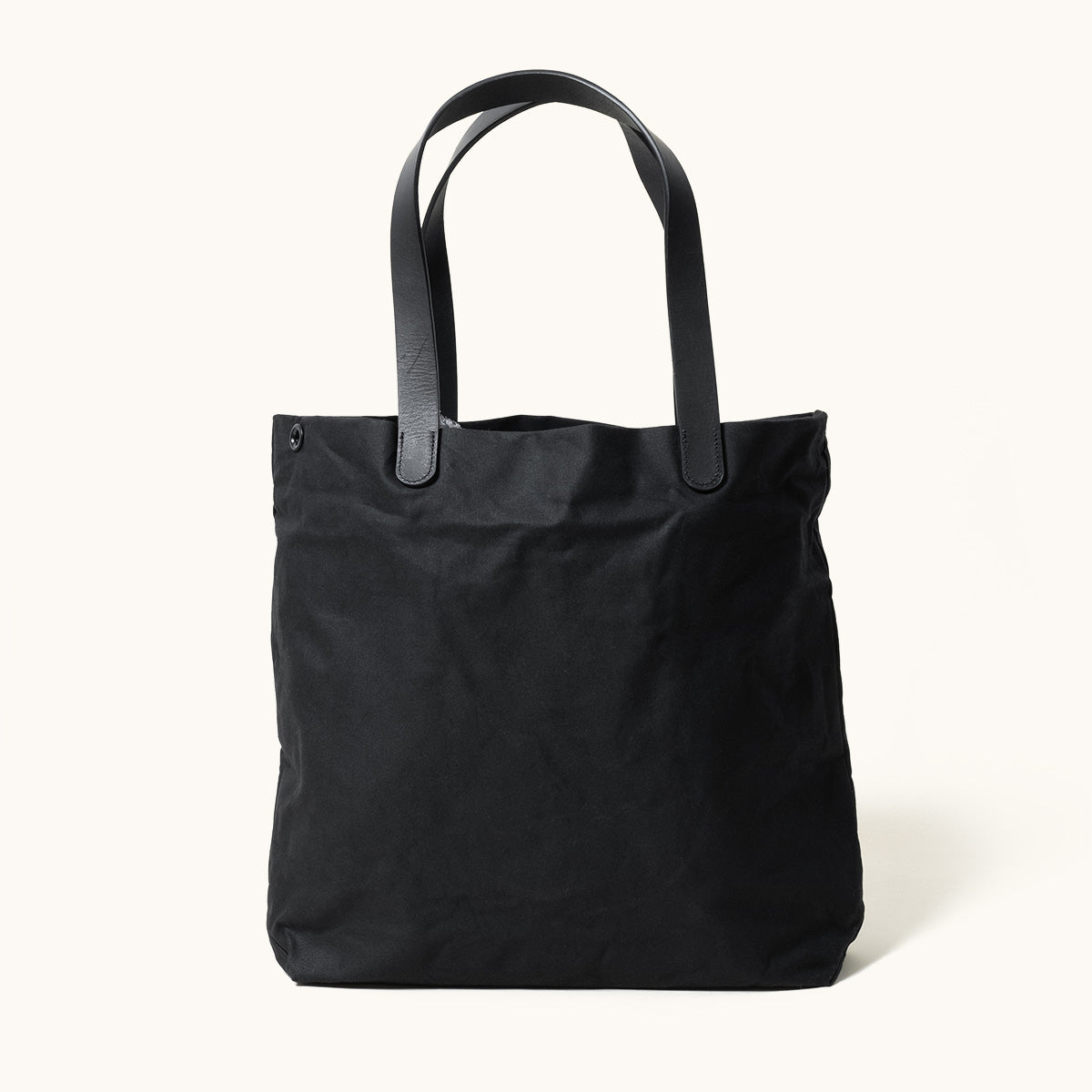 Black waxed canvas tote bag with black leather handles and a snap closure.