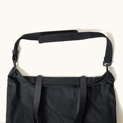 Black waxed canvas Simple Tote with an adjustable webbed shoulder strap and smooth leather tote handles, cropped view.