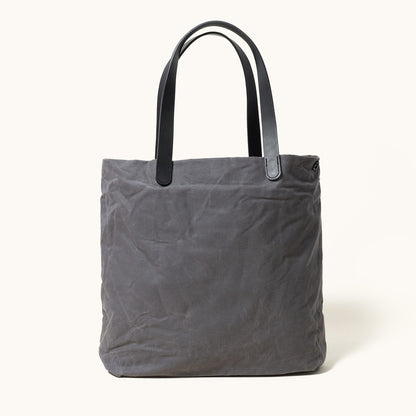 Slate grey waxed canvas tote bag with black leather handles and visible creases.
