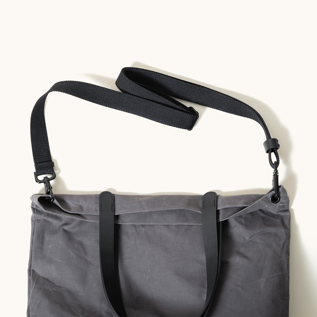 Slate grey waxed canvas tote bag with black leather handles and a detachable black webbing strap.