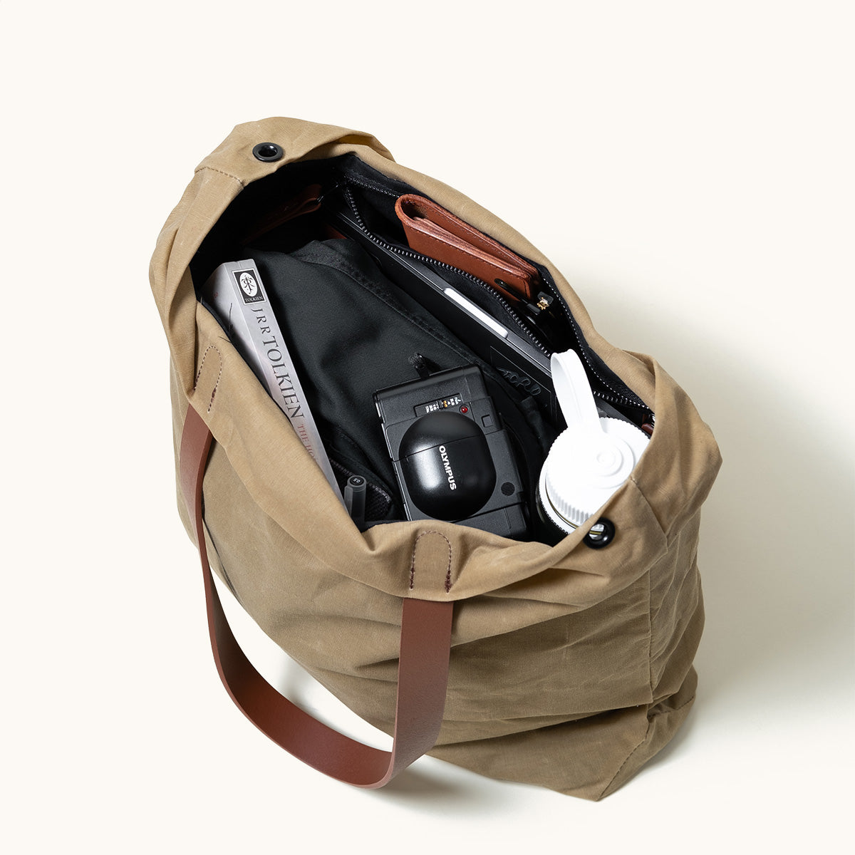 Tan waxed canvas tote bag with brown leather straps, open and filled with everyday items.