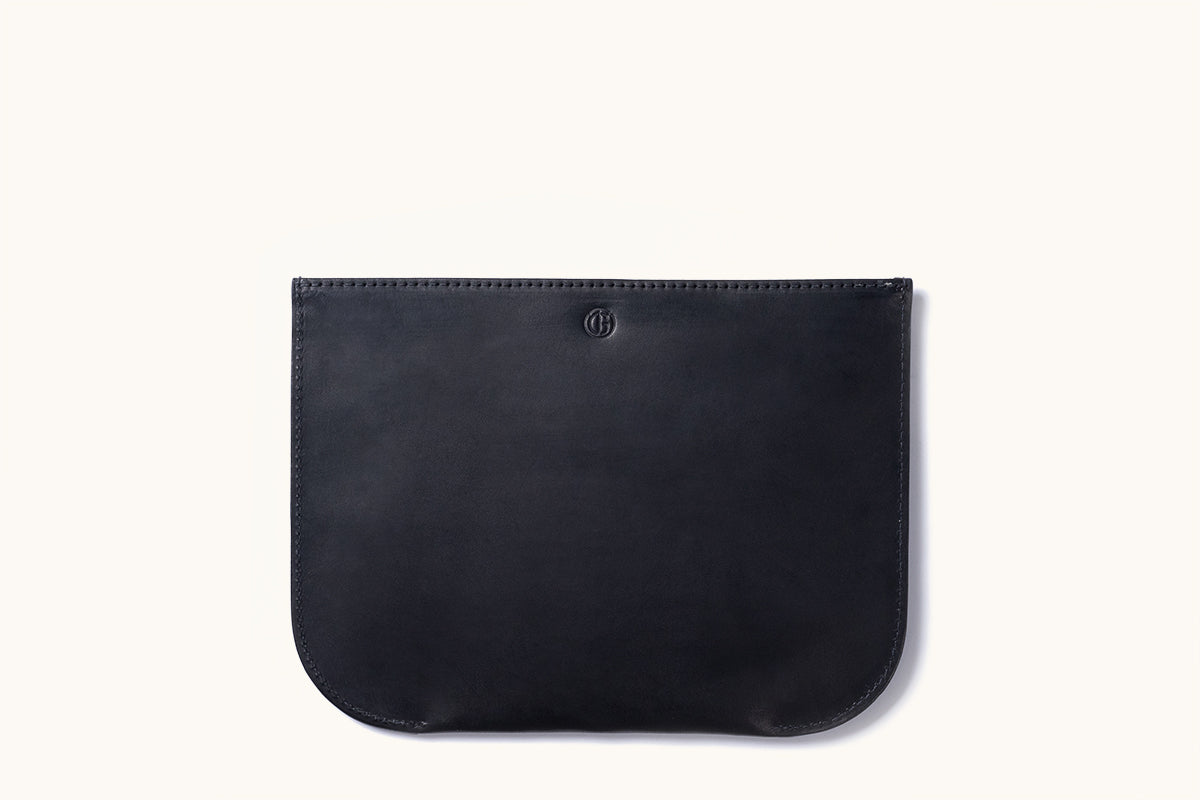 Black leather zip pouch with a debossed circular logo, stitched edges, and rounded bottom corners, laid flat.